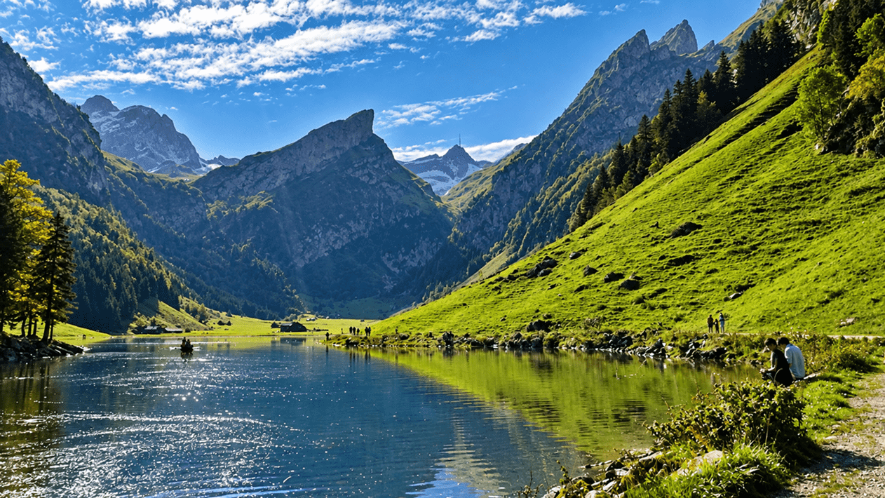 Seealpsee inmitten der beeindruckenden Schweizer Berglandschaft mit grünen Alpwiesen, schroffen Felsgipfeln, Wald und blauem Himmel.
