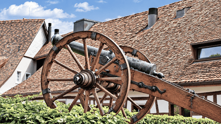 Historische Kanone auf einem hölzernen Rädergestell vor den traditionellen Ziegeldächern der Altstadt von Regensberg im Kanton Zürich.